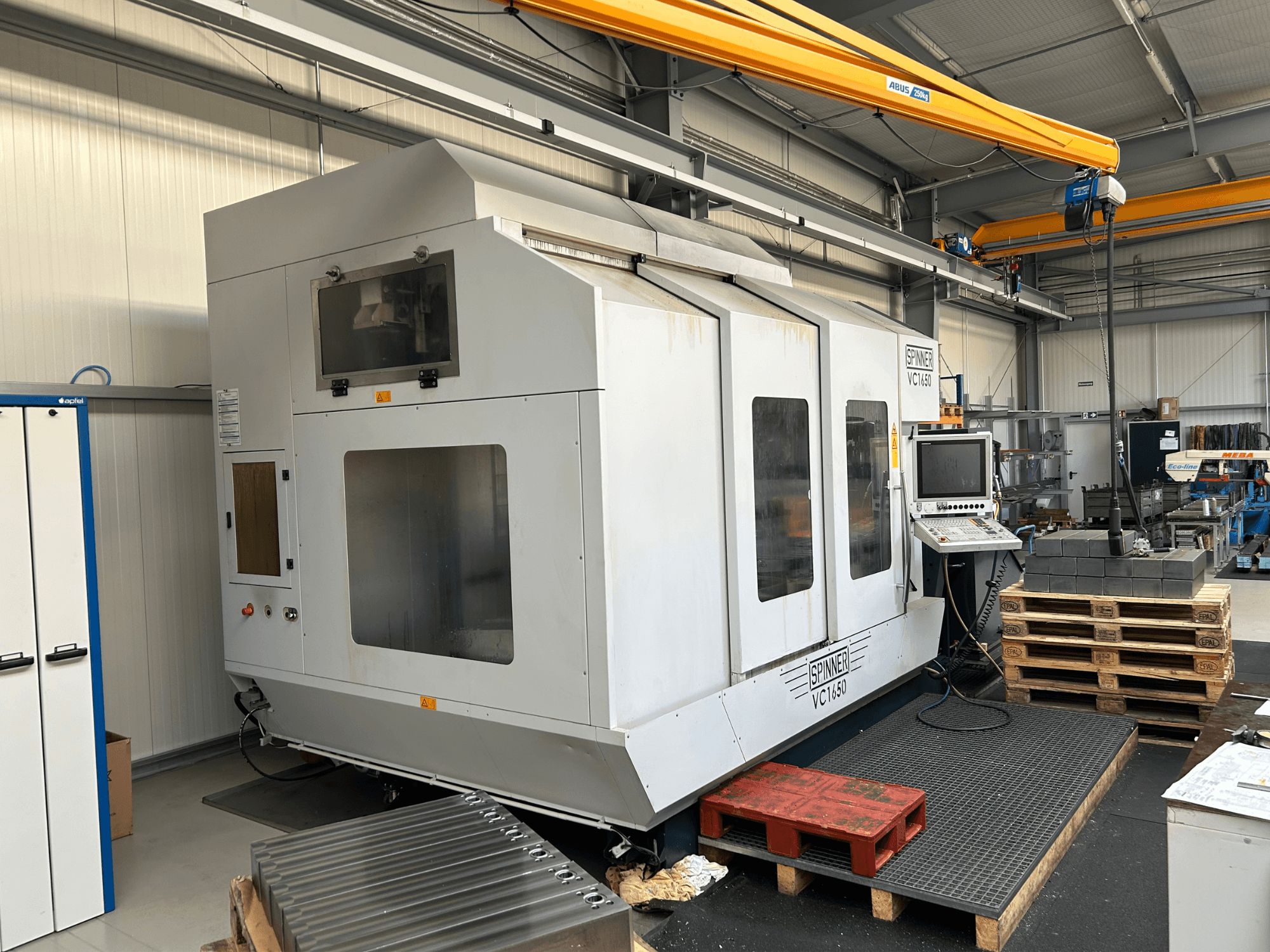 Spinner VC 1650 CNC machine, front view, with control panel, large windows, and pallets stacked nearby in a workshop setting.