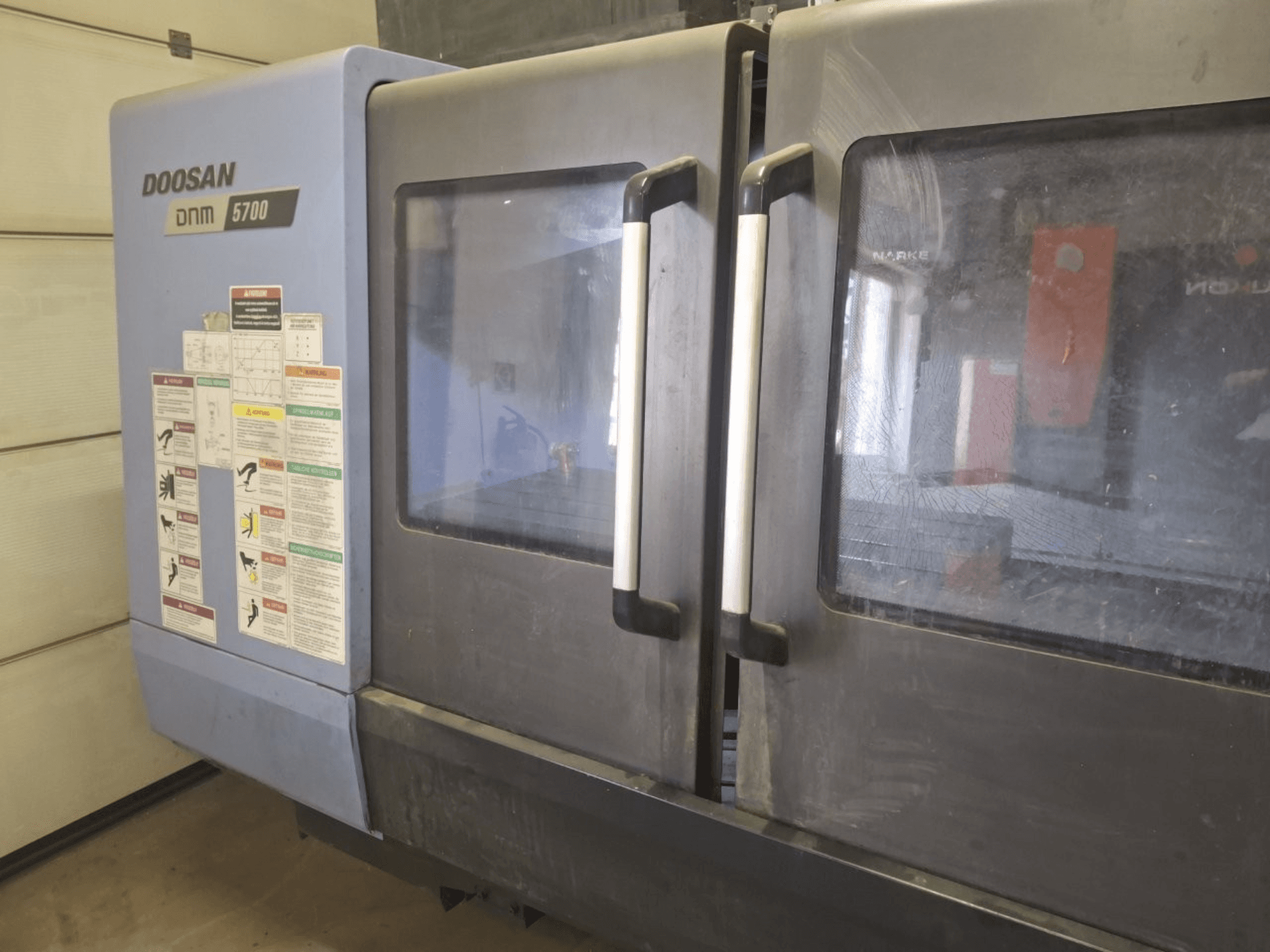 Front view of a DOOSAN DNM 5700 Vertical Machining Centre, showcasing dual doors and control panels with operational guidelines.