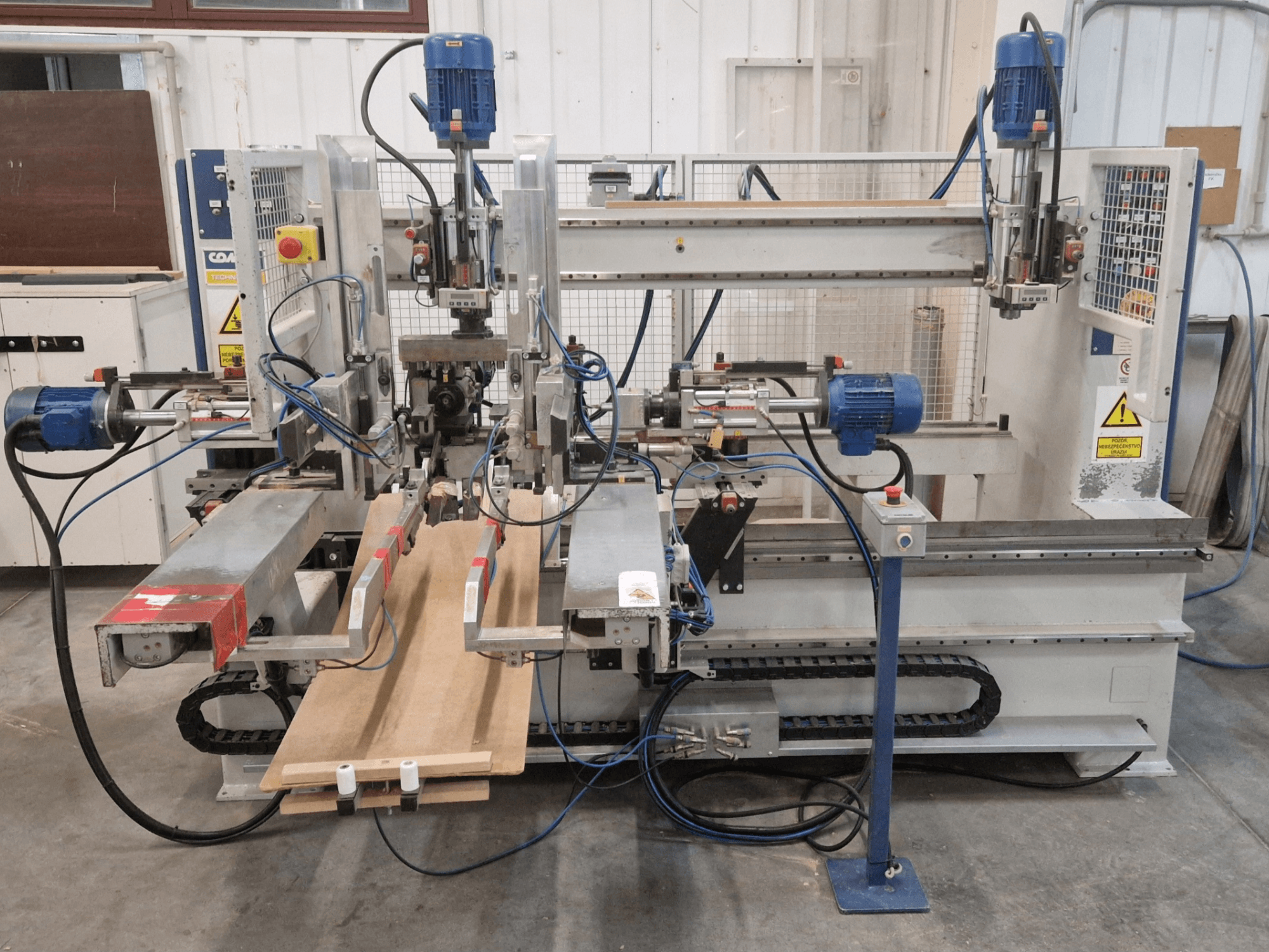 COMEC FMOV 1500 multi-spindle drilling machine front view, showing dual spindles, control panel, and wood piece in operation.
