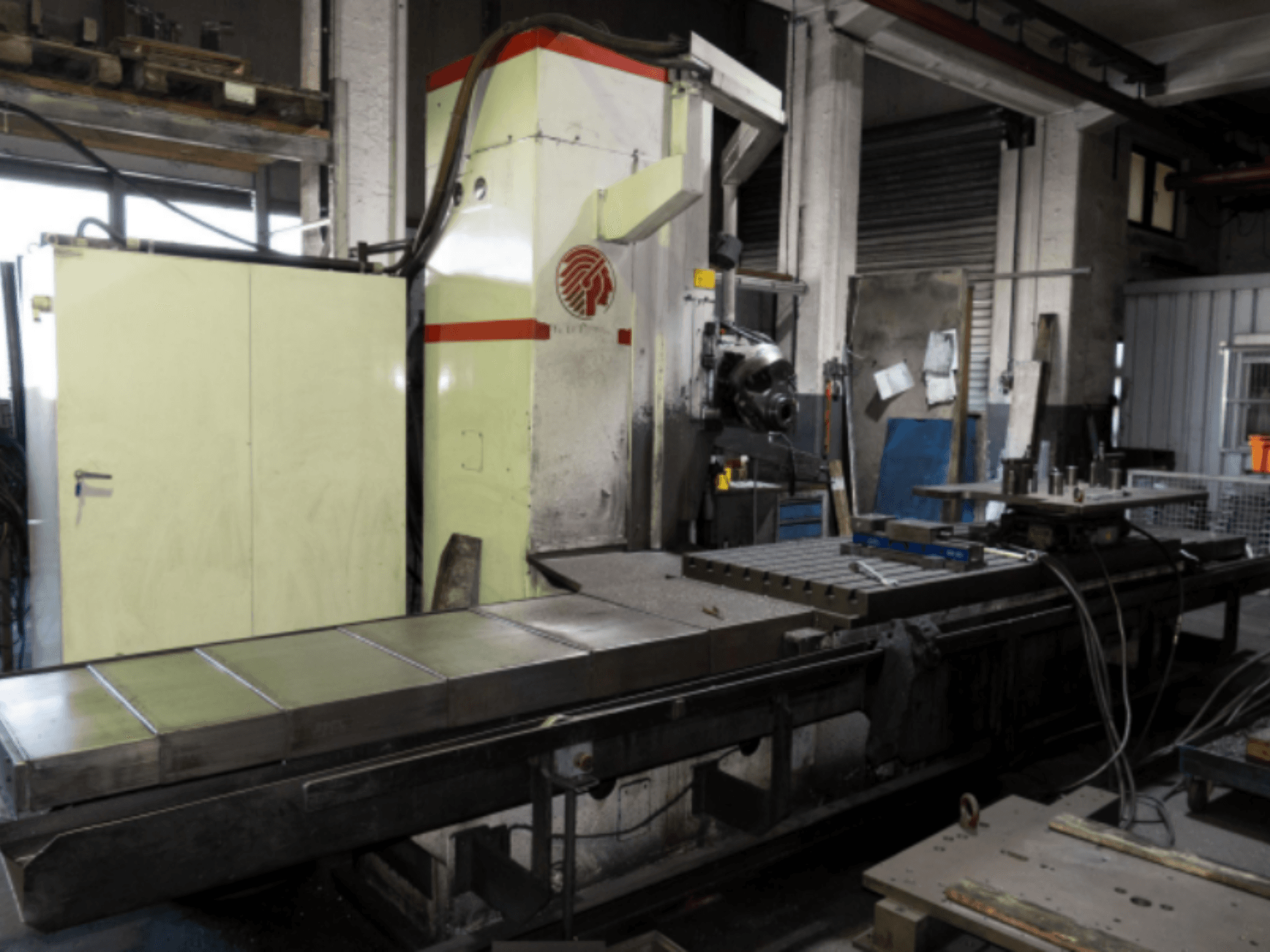 Industrial milling machine with a large table, side view, showcasing controls and attachments in a workshop setting.