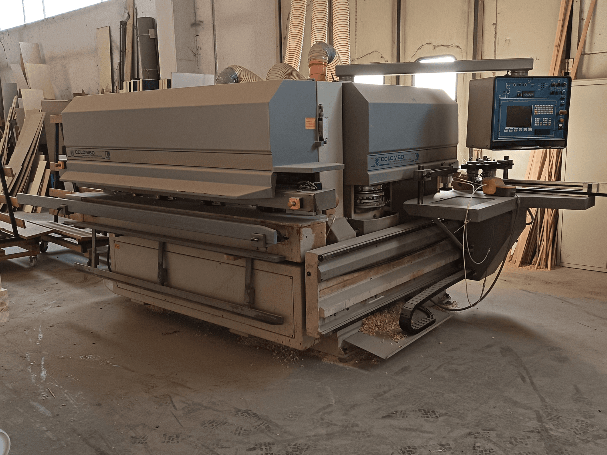 Colombo woodworking machine, side view, showcasing control panel, cutting blades, and saw dust accumulation in workshop.