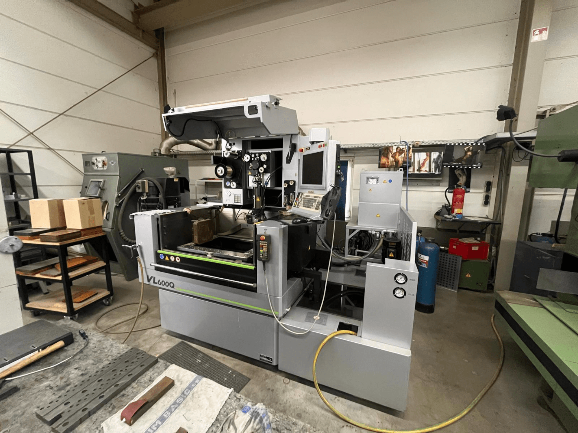 VL600Q CNC machine in a workshop, front view, with control panel, material in place, and various tools nearby.