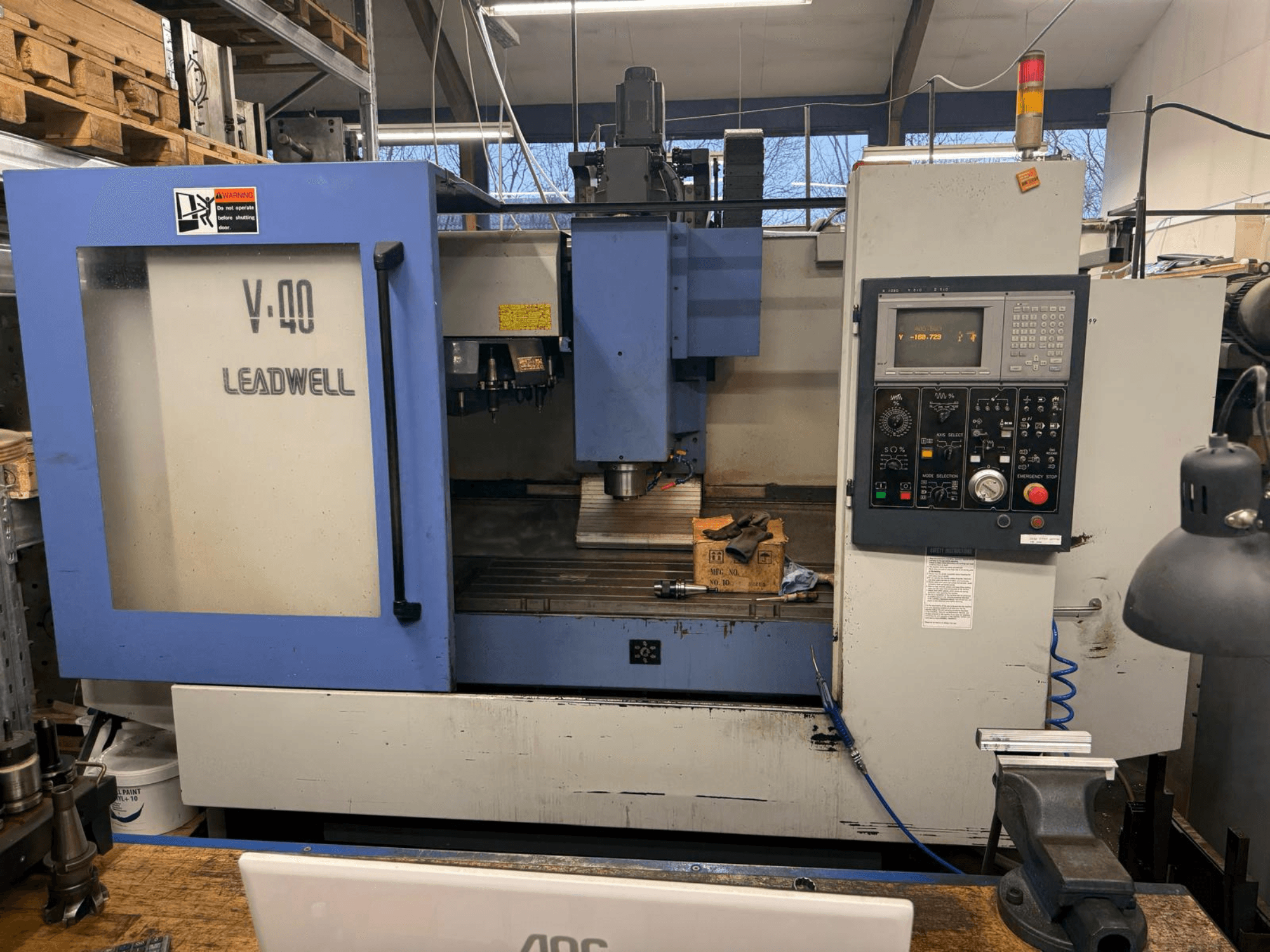 LEADWELL V-40 CNC milling machine, front view, featuring a control panel, cutting tools, and a vise on a workbench.