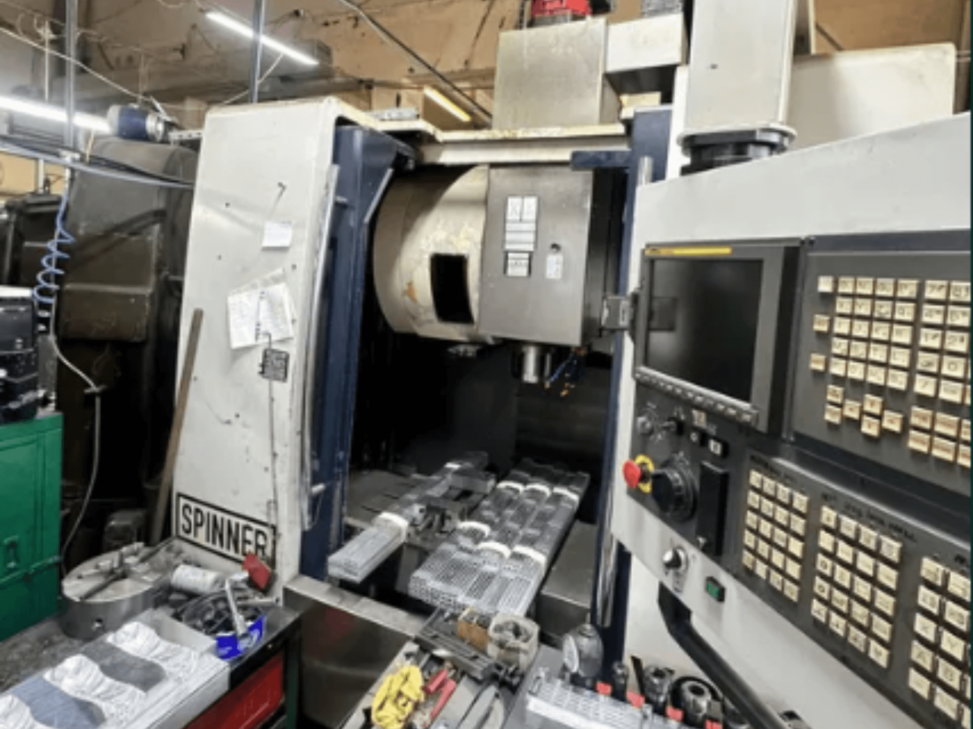 CNC machine by Spinner, front view; features touchscreen interface, tools on workspace, and machined parts ready for processing.
