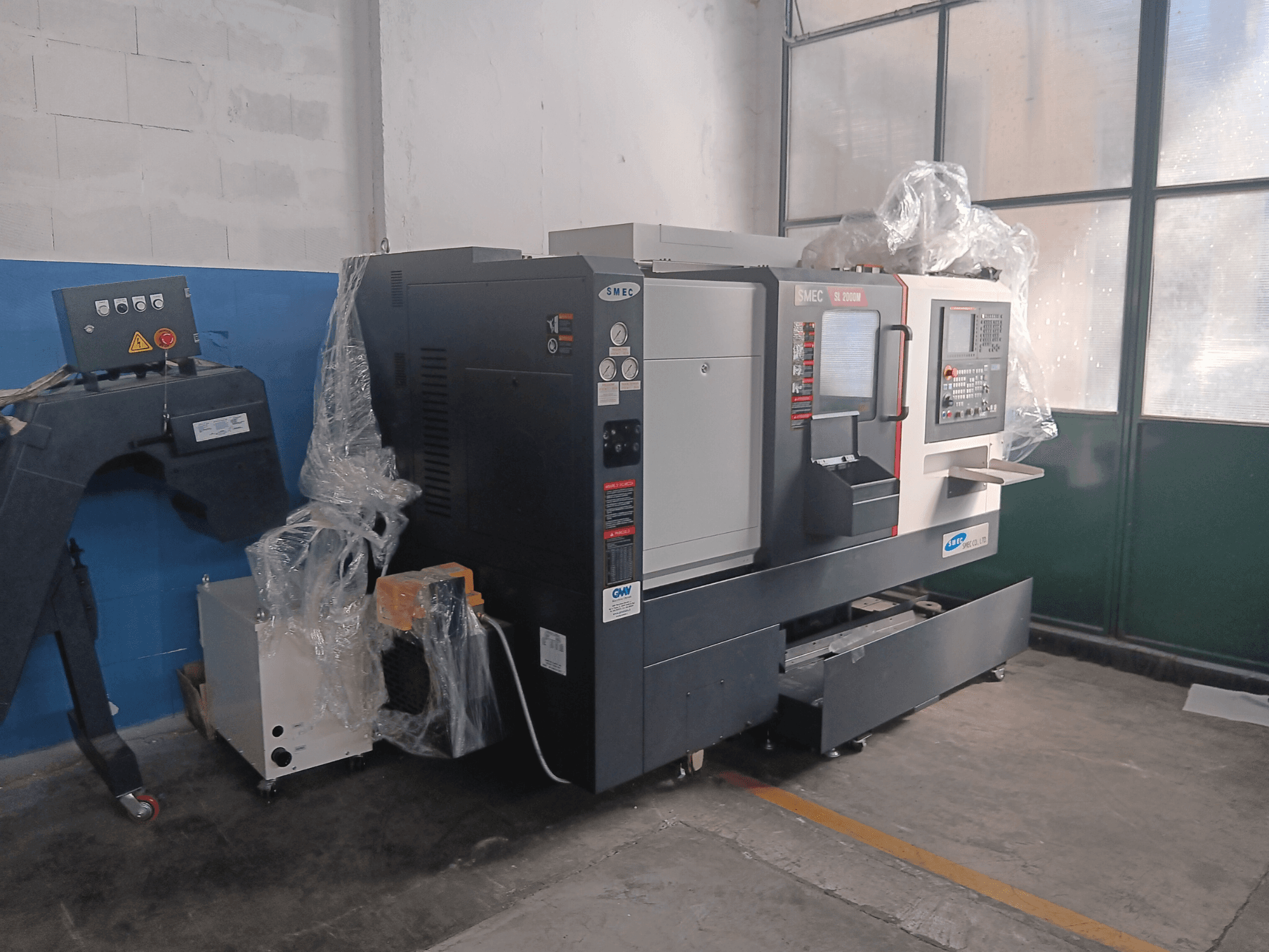 SMEC SL2000M B TYPE horizontal turning machine, side view, featuring control panel and protective plastic wrap.