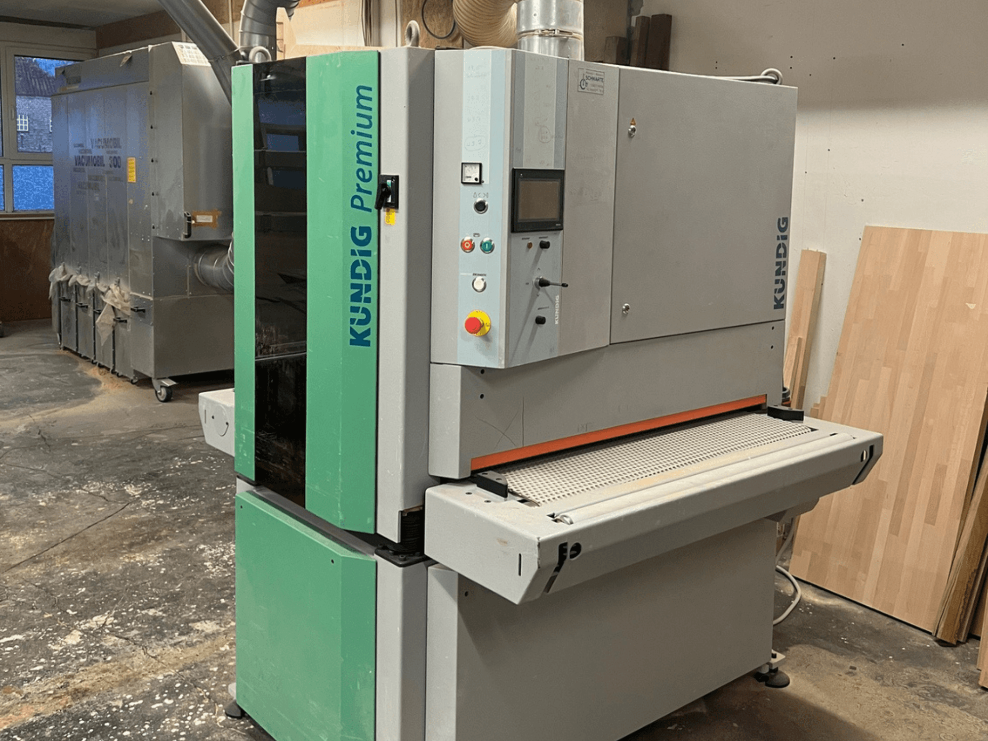 Kundig Premium-1 1100K belt sander in gray and green, shown in a side view with control panel and sanding belt visible.