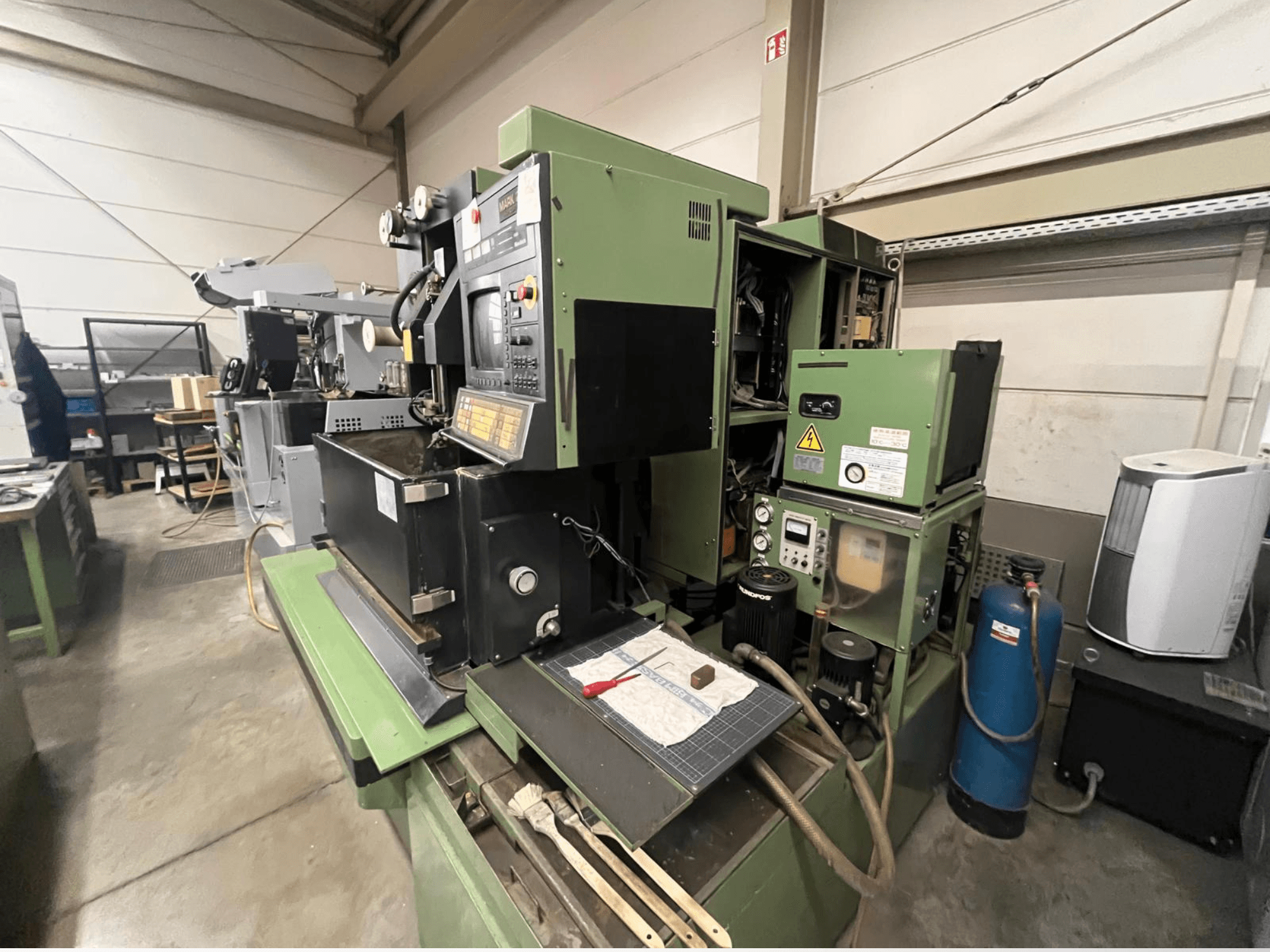 Green industrial machine with control panel, side view; includes hydraulic components and workspace surface with tools.