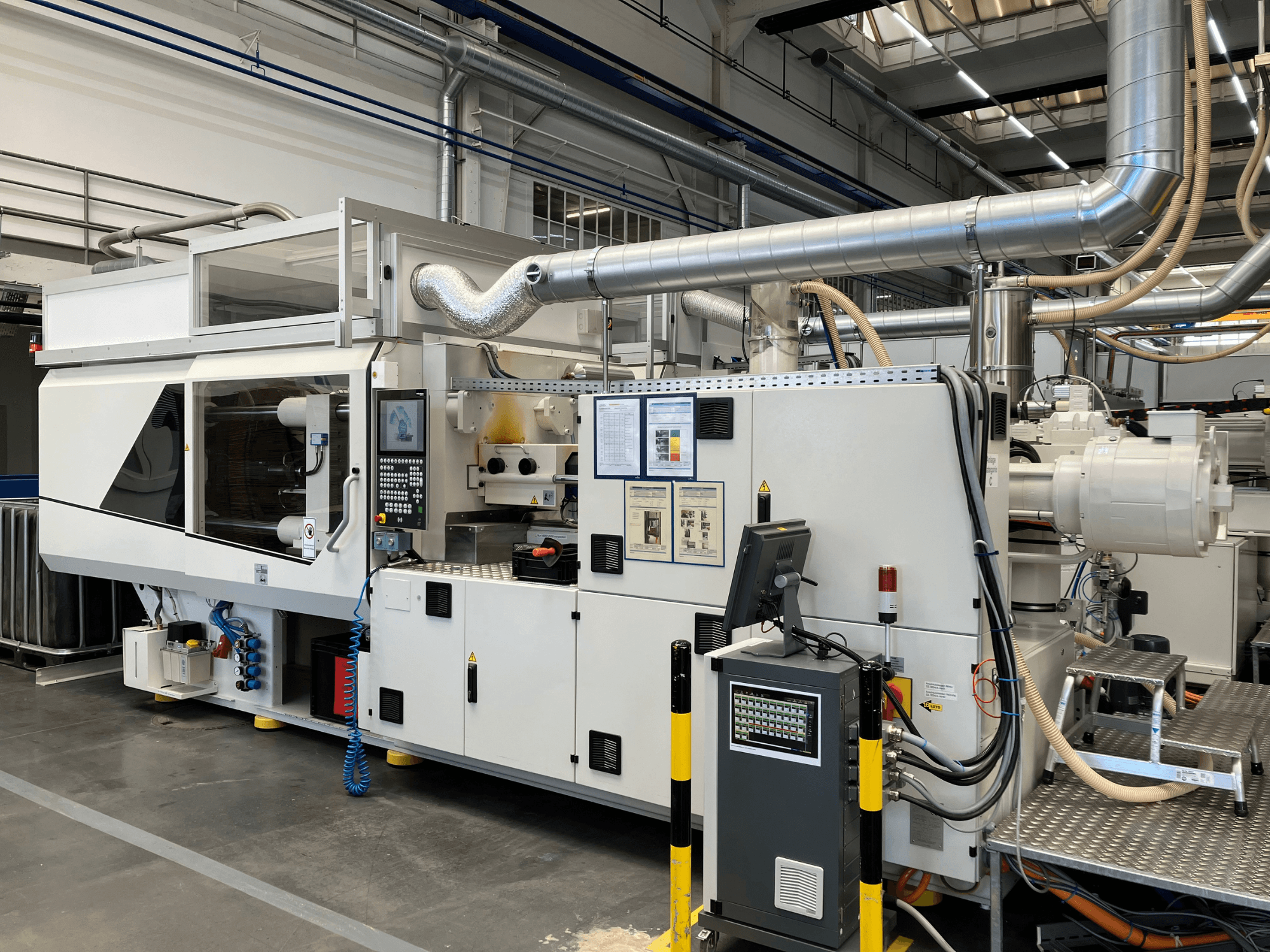 Front view of an industrial machine with control panel, pipes, and display screens, featuring a sleek white design and technical details.