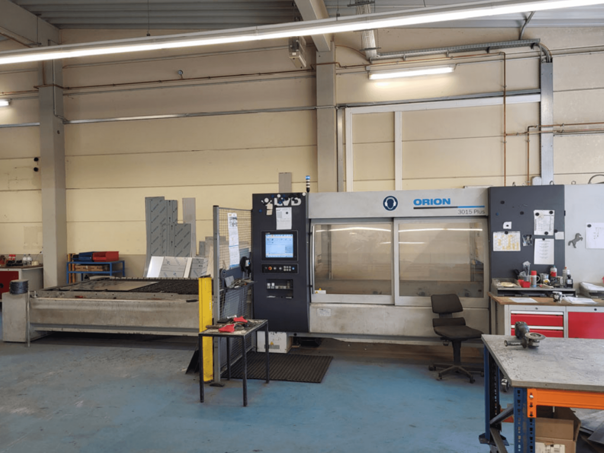 ORION 3015 Plus cutting machine in a workshop, front view, featuring control panel and surrounding worktables.