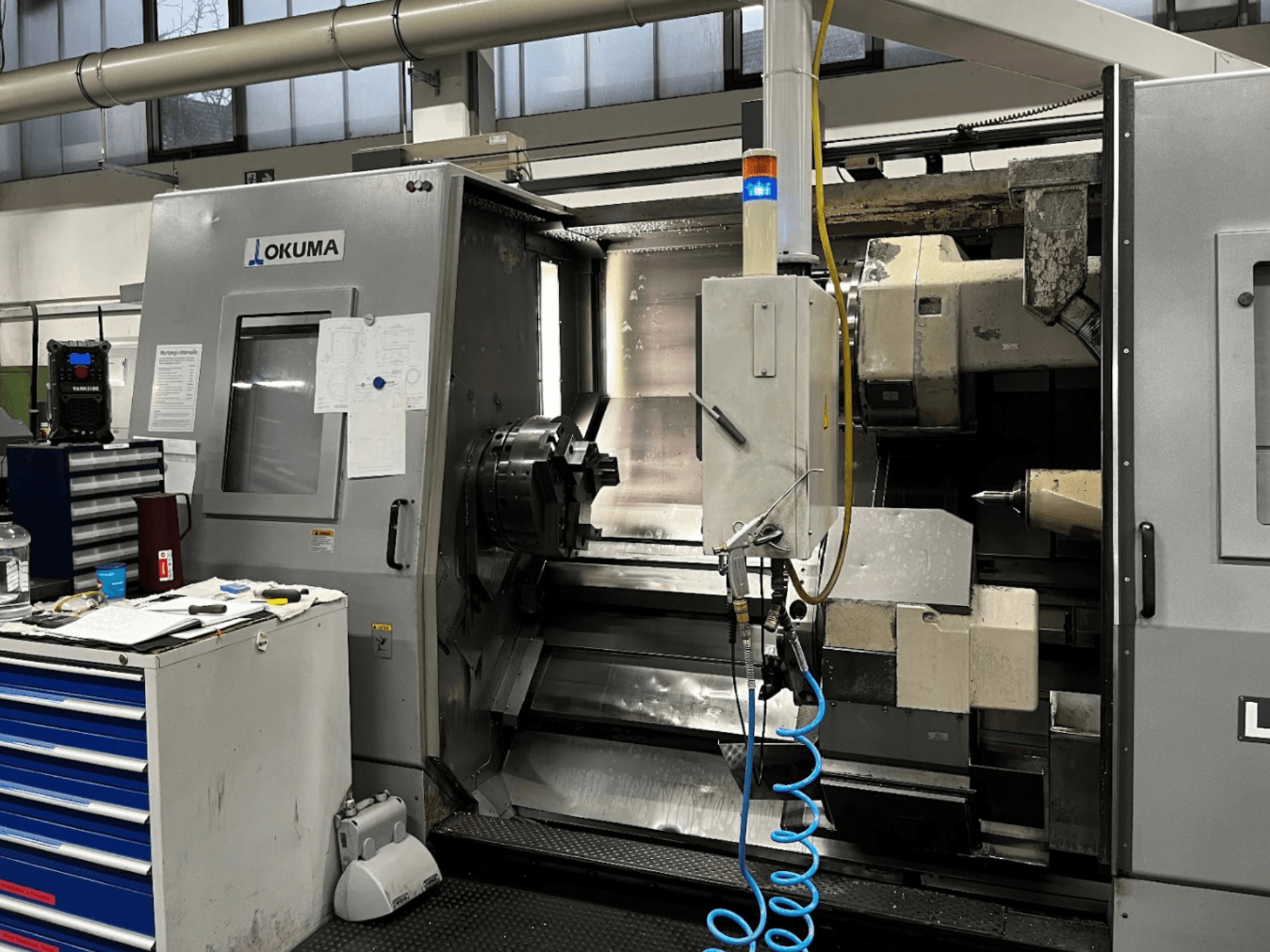 Okuma LU35-M horizontal turning machine, front view. Features control panel, tools, and large chuck for machining operations.